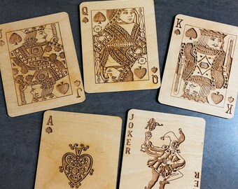 May include: Five wooden playing cards with a black spade suit. The cards are the Queen, King, Ace, and Joker. The Joker card has the word "Joker" written vertically on both sides.