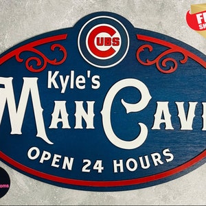 May include: A blue and red wooden sign with the text "Kyle's Man Cave Open 24 Hours". The sign features a white cursive font and a red and white circular logo with the text "CUBS" in white.