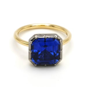 Op de afbeelding: Een gouden ring met een grote, rechthoekige, blauwe edelsteen gezet in een zilveren zetting.
