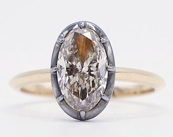 May include: A gold ring with an oval-shaped diamond set in a silver bezel. The diamond has a light brown hue.