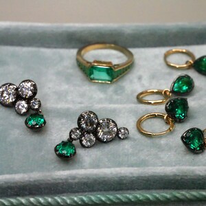 May include: A collection of gold and black jewelry featuring emerald and diamond accents. The jewelry includes a ring, earrings, and a pendant.