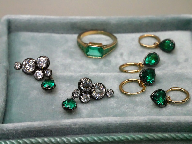 May include: A collection of gold and black jewelry featuring emerald and diamond accents. The jewelry includes a ring, earrings, and a pendant.