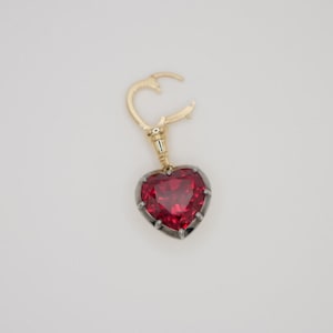 May include: A heart-shaped ruby pendant with a gold and silver setting. The pendant is attached to a gold chain with a clasp.