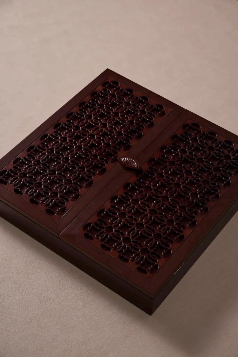 May include: A dark brown wooden box with a decorative floral pattern carved into the lid. The box has a rectangular shape and a small, fan-shaped handle. The wood has a rich, warm tone.