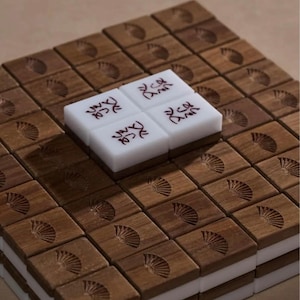 May include: A set of wooden Mahjong tiles with a fan design carved into the wood. Four white tiles with red characters are stacked on top of the wooden tiles. The tiles are arranged in a grid pattern.
