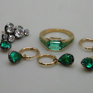 May include: A set of emerald green and diamond jewelry featuring a ring with a large emerald green stone, a pair of earrings with emerald green stones, and a pair of hoop earrings with emerald green stones.