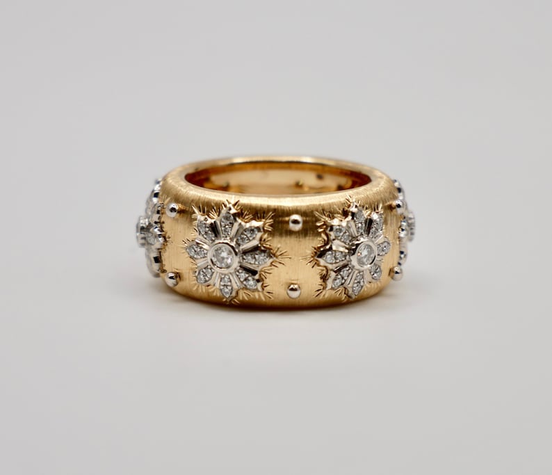 Puede incluir: Un anillo ancho de oro con acabado cepillado, adornado con dise&ntilde;os florales con diamantes y peque&ntilde;os detalles plateados. El anillo tiene una banda de aproximadamente 1,9 cm de ancho, mostrando una mezcla de texturas y materiales preciosos.
