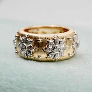 Puede incluir: Un anillo ancho de oro con una superficie texturizada, adornado con dise&ntilde;os en forma de copo de nieve. Cada copo de nieve presenta un diamante central y piedras m&aacute;s peque&ntilde;as. Peque&ntilde;as cuentas plateadas est&aacute;n intercaladas alrededor del anillo.