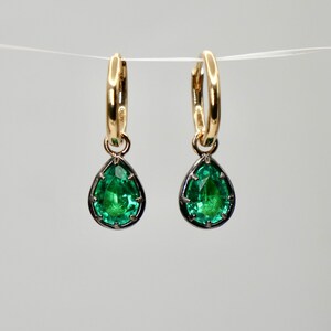 May include: A pair of gold hoop earrings with a teardrop-shaped green gemstone pendant hanging from each hoop.