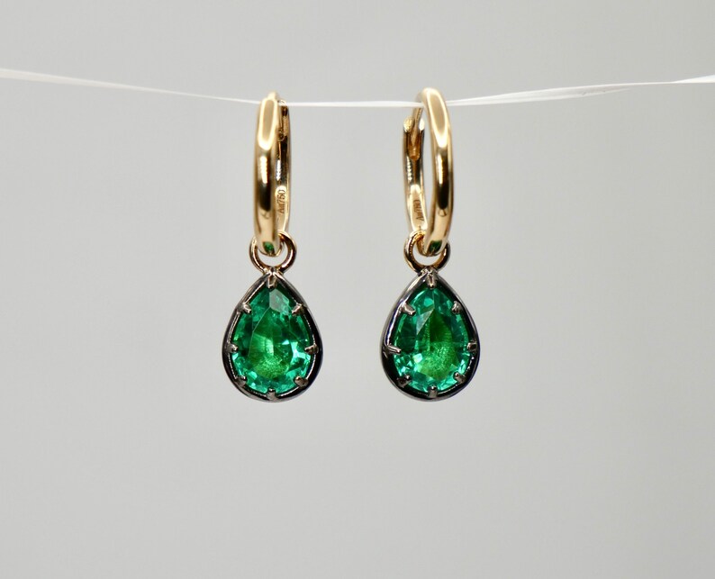 May include: A pair of gold hoop earrings with a teardrop-shaped green gemstone pendant hanging from each hoop.