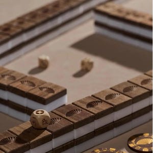 May include: A wooden Mahjong set with brown tiles and white inserts. The tiles are arranged in a game layout, with dice and decorative chips visible. The tiles have a fan design carved into them. The game is set on a neutral surface.