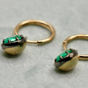 May include: A pair of gold hoop earrings with a green gemstone set in a black metal bezel.