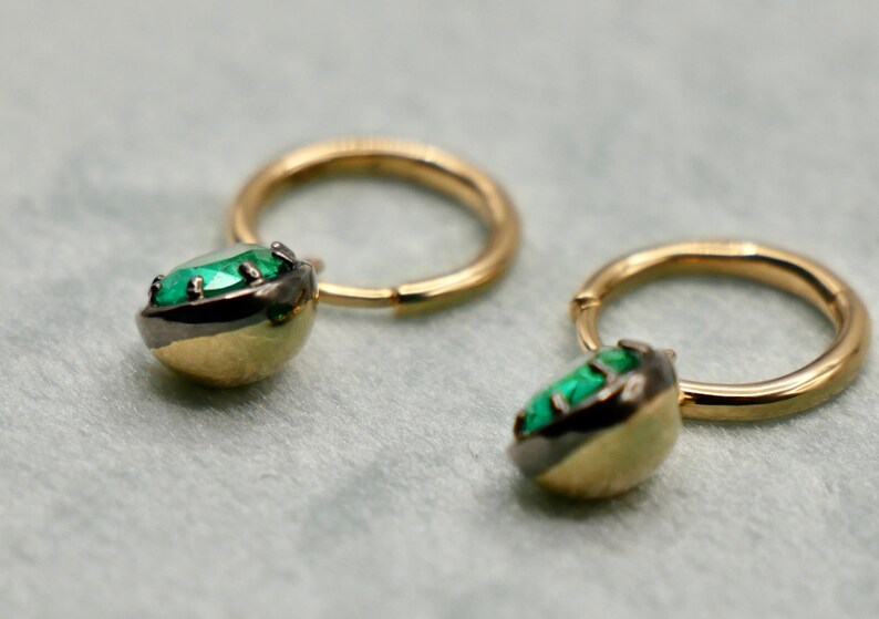 May include: A pair of gold hoop earrings with a green gemstone set in a black metal bezel.