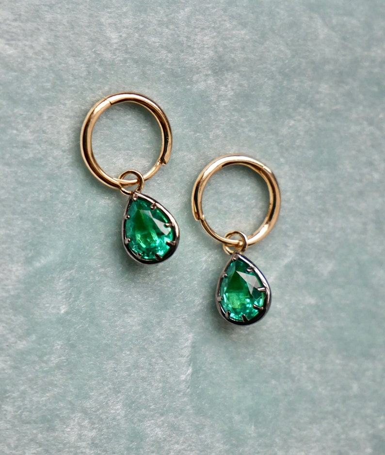 May include: A pair of gold hoop earrings with a teardrop-shaped green gemstone pendant hanging from each hoop.
