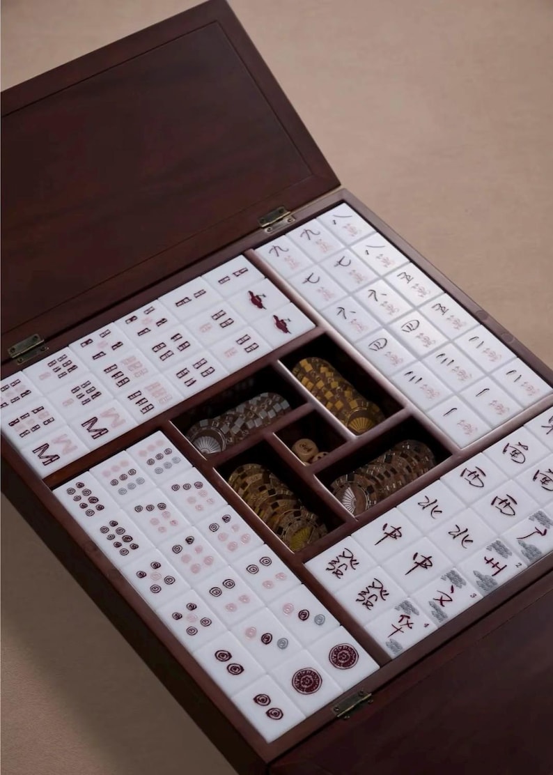 May include: A wooden Mahjong set with a dark brown finish. The open box reveals tiles with red and black symbols, along with wooden and decorative pieces. The tiles are arranged in compartments within the box.