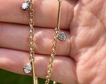 May include: A gold chain necklace with three diamond charms: a round charm, a pear-shaped charm, and a heart-shaped charm.