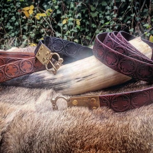 May include: Two leather belts with intricate embossed designs and brass buckles. The belts are brown and black and are lying on a furry surface.