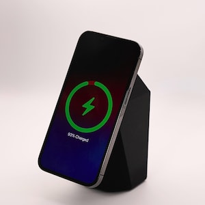 May include: A black smartphone rests on a black geometric charging stand. The phone screen displays a green charging symbol and the text "93% Charged" against a blue and red gradient.