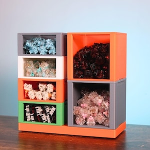 Könnte beinhalten: Ein Mehrfach-Fach-Organizer in Orange, Grau, Weiß und Grün, gefüllt mit verschiedenen mechanischen Tastaturschaltern. Die Schalter sind in Blau-, Braun-, Klar- und Rosatönen gehalten. Der Organizer dient zum Halten und Präsentieren der Schalter.