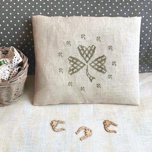 May include: A beige linen pillow with a green embroidered shamrock design. Three wooden horseshoe charms with shamrock accents are in the foreground.