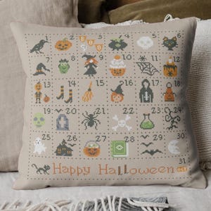 K&ouml;nnte beinhalten: Ein beiges Kissen mit einem Kreuzstich-Design mit 31 Halloween-Motiven, die von 1 bis 31 nummeriert sind. Die Motive umfassen einen Geist, eine Hexe, eine Spinne, einen K&uuml;rbis, einen Sch&auml;del, einen Kessel und eine Fledermaus. Das Kissen hat auch den Text "Happy Halloween" und "31 OCT" aufgedruckt.