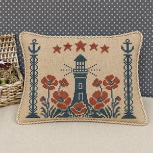 May include: Rectangular beige pillow with a nautical cross-stitch design. Features a blue lighthouse, red poppies, and blue anchor accents. The pillow is bordered with a rope trim and has a dotted background.