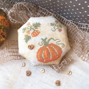 May include: A white fabric pumpkin pincushion with orange and green embroidery. The pincushion is surrounded by small wooden buttons.