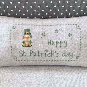 May include: A beige linen pillow with a green embroidered design featuring a leprechaun and the text "Happy St. Patrick's Day".