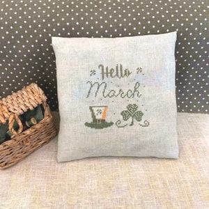 May include: A white pillow with the text "Hello March" embroidered on it. The pillow also features a green shamrock and a green leprechaun hat.