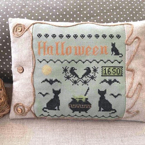 May include: A green and black embroidered cushion featuring the word "Halloween" and a black cat, bats, and a cauldron with a bubbling potion. The cushion is edged with brown rope trim and has two brown buttons.