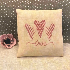May include: A beige linen cushion with a red embroidered heart and the word "love" in cursive.