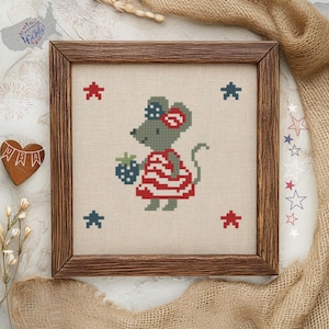 Könnte beinhalten: Kreuzstich-Kunstwerk einer Maus in einem rot-weiß gestreiften Kleid, die eine Brombeere hält. Das gerahmte Stück hat rote und blaue Sterne um die Maus herum. Das Kunstwerk befindet sich in einem Holzrahmen.