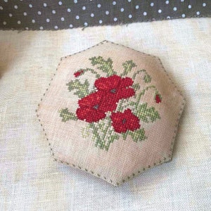 May include: A hexagonal-shaped needlepoint cushion with a cross-stitch design of red poppies and green leaves.