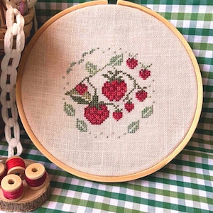 May include: A close-up of a finished embroidery hoop with a design of red strawberries and green leaves on a white linen fabric. The hoop is made of wood and has a natural finish.