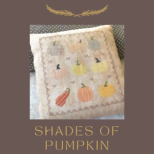 May include: A beige pillow with a cross-stitch design of various shades of pumpkins. The pillow is decorated with a brown border and the text "Shades of Pumpkin" is written below the pillow.