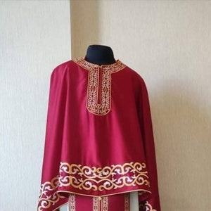 May include: A burgundy liturgical robe with gold embroidery. The robe has a high collar and long sleeves. The embroidery is intricate and features a floral design.