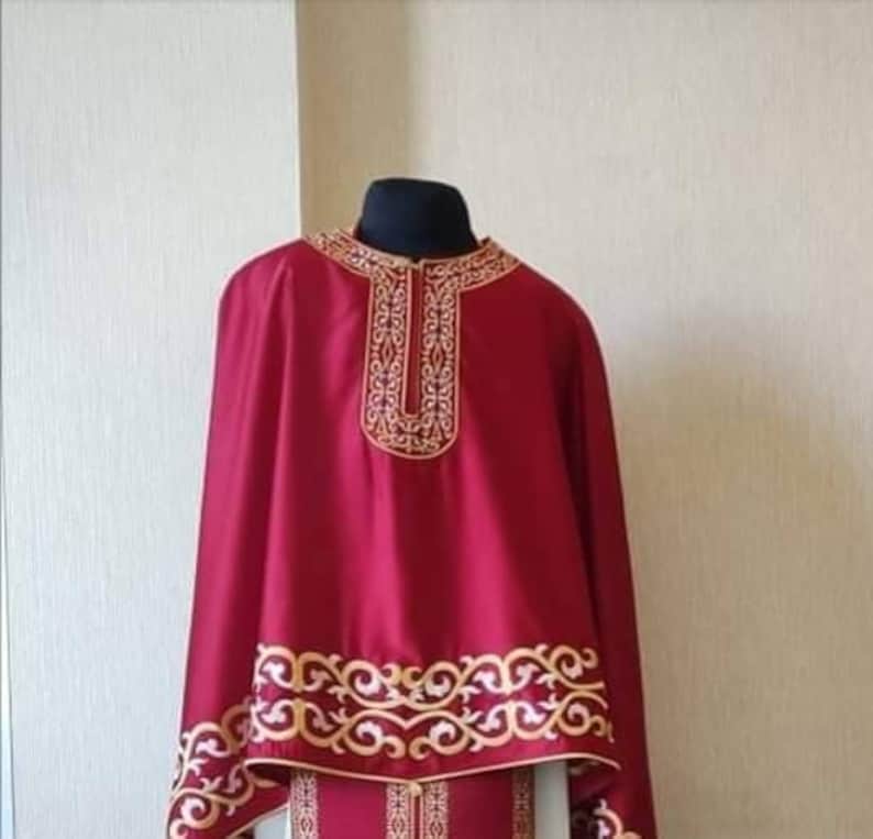 May include: A burgundy liturgical robe with gold embroidery. The robe has a high collar and long sleeves. The embroidery is intricate and features a floral design.