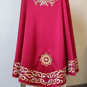 May include: A red liturgical vestment with gold embroidery. The vestment features a cross and floral designs. The bottom of the vestment has a white trim with gold embroidery.