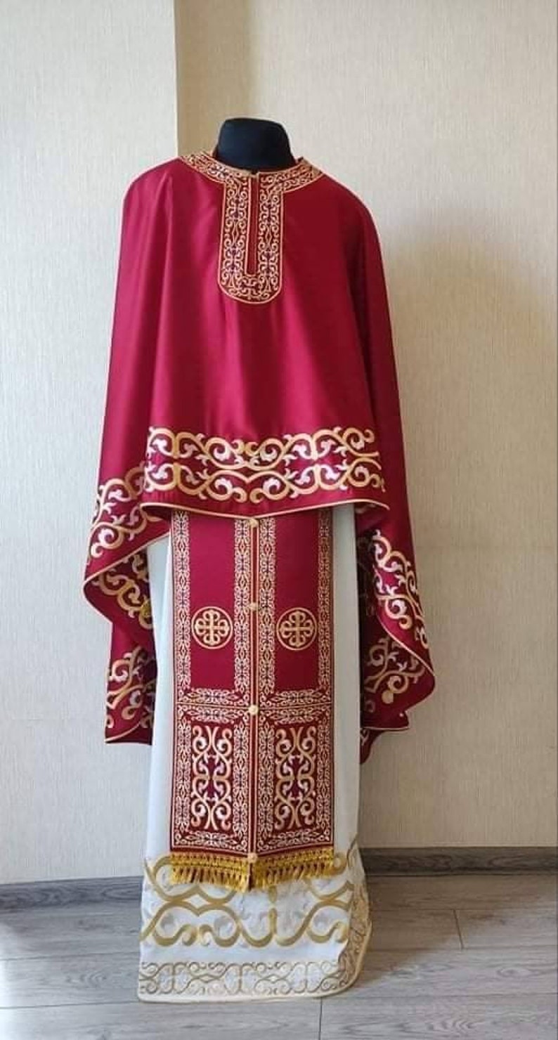 May include: A red and gold liturgical vestment with intricate embroidery. The vestment features a long, flowing robe with a decorative collar and a matching stole.