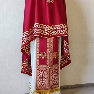May include: A red and white liturgical vestment with gold embroidery. The vestment has a long, flowing robe with a shorter, cape-like piece on top. The embroidery features intricate floral patterns.