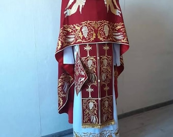 Könnte beinhalten: Ein rotes liturgisches Gewand mit goldener Stickerei, die Engel und Blumenmotive zeigt. Das Gewand hat ein weißes Untergewand mit einem goldenen Stickrand.