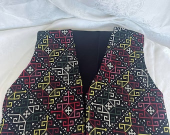 Puede incluir: Un chaleco negro con un patrón geométrico bordado en hilo rojo, amarillo y verde.