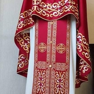 May include: A red and white liturgical vestment with gold embroidery. The vestment has a long, flowing robe with a shorter, cape-like piece on top. The embroidery features intricate floral patterns and crosses.