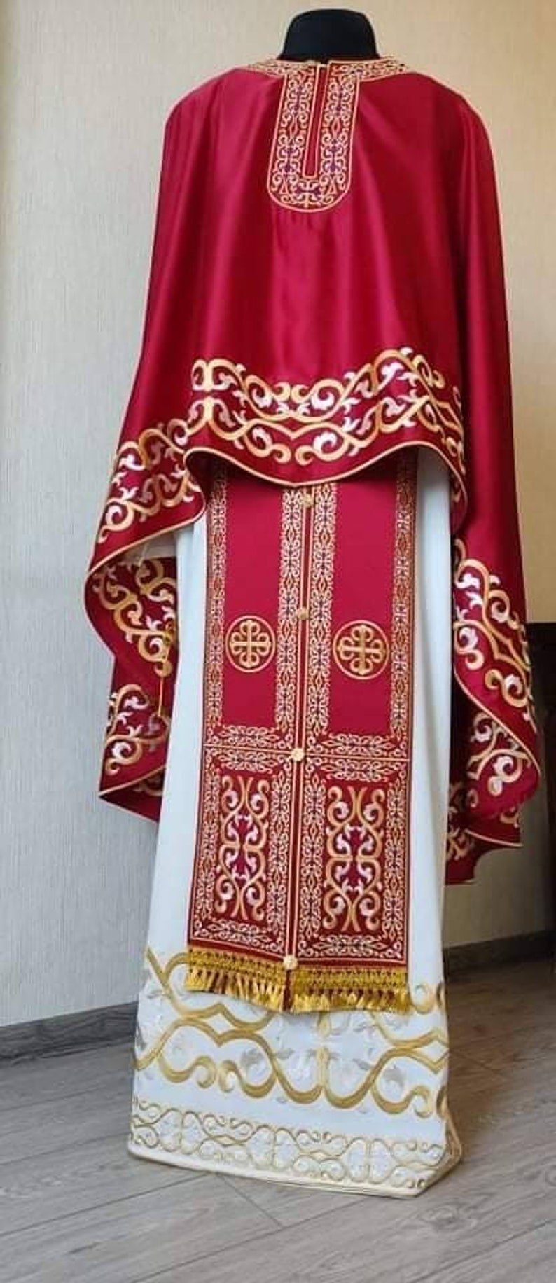 May include: A red and white liturgical vestment with gold embroidery. The vestment has a long, flowing robe with a shorter, cape-like piece on top. The embroidery features intricate floral patterns and crosses.