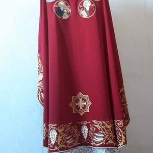 May include: A red liturgical vestment with gold embroidery. The vestment features a cross and floral designs. There are also several circular images of saints embroidered on the back.