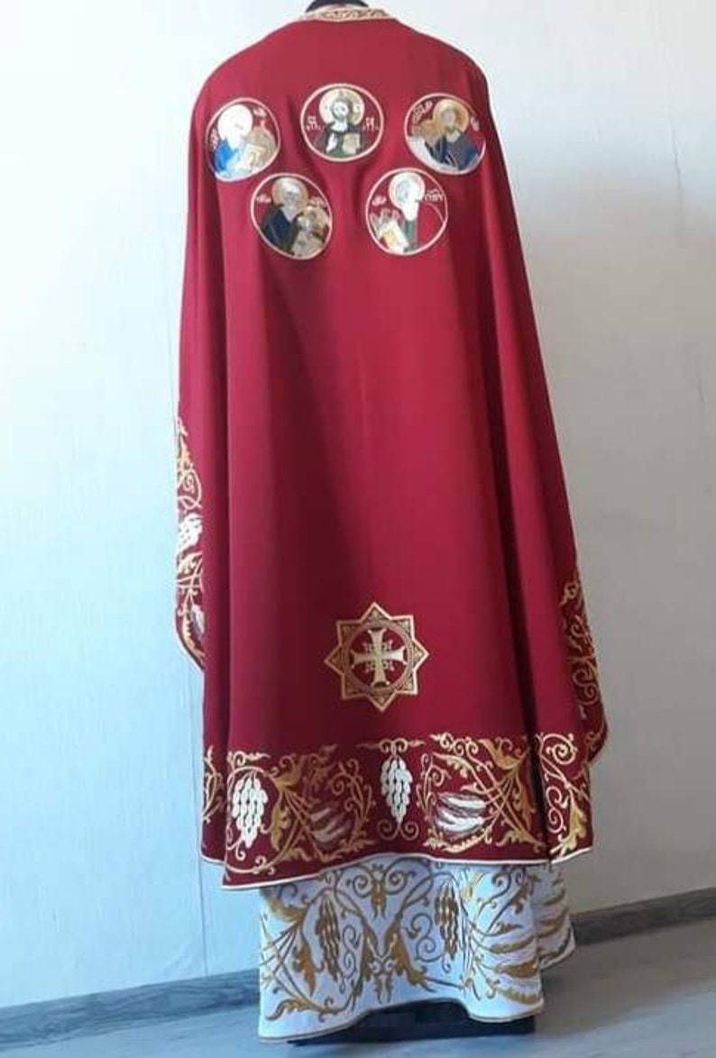 May include: A red liturgical vestment with gold embroidery. The vestment features a cross and floral designs. There are also several circular images of saints embroidered on the back.