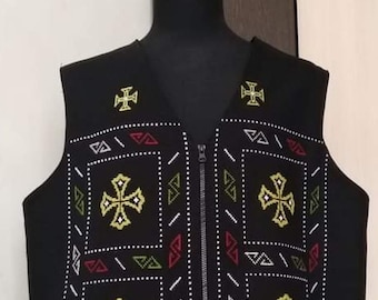 Puede incluir: Chaleco negro con cierre de cremallera y patrones geométricos bordados en blanco, rojo, verde y amarillo. El patrón presenta un diseño de cruz repetido.