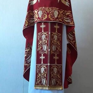 May include: A red and white liturgical vestment with gold embroidery. The vestment features a design of angels and grapevines.