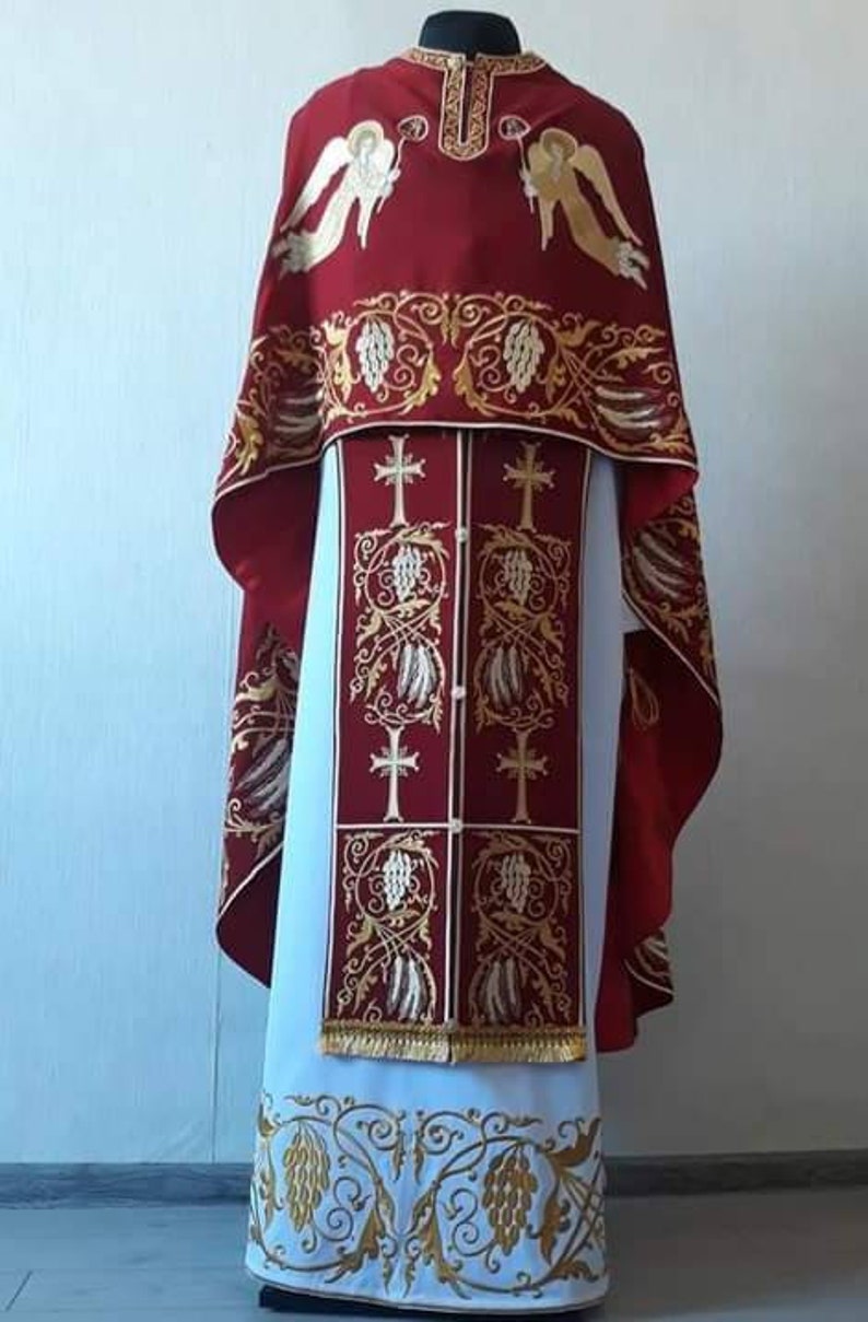 May include: A red and white liturgical vestment with gold embroidery. The vestment features a design of angels and grapevines.