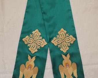 May include: A green liturgical stole with gold embroidery of angels and crosses. The stole has gold fringe at the ends.